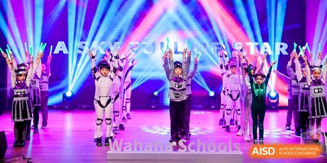 Students dressed in astronaut-style costumes perform a high-energy dance under stage lights at Wahaha International School.