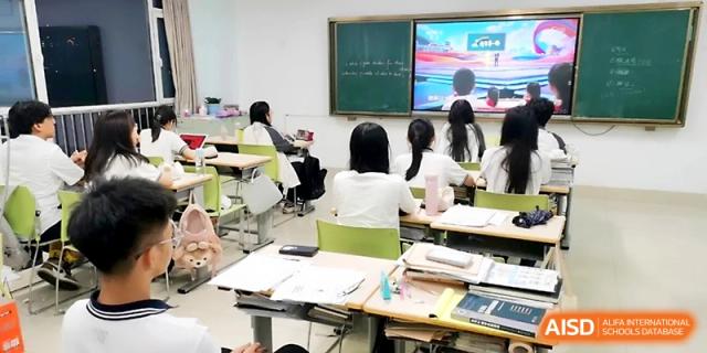 Students sit at desks in a bright classroom, facing a digital screen showing a colorful presentation during a lesson at WeiFang No.1 Middle School.