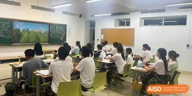 Students in white shirts sit at their desks in a classroom, listening to a lecture with green chalkboards on the wall at WeiFang No.1 Middle School.