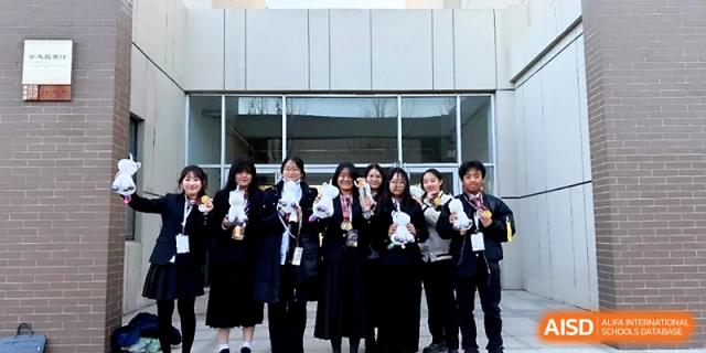 A group of students in dark uniforms stand outside a building holding certificates and awards they have won at WeiFang No.1 Middle School.