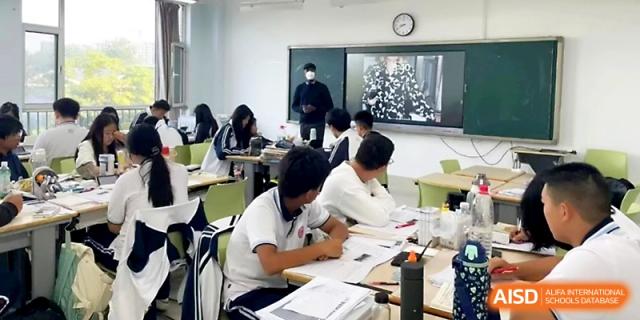 Students in white uniforms sit in a modern classroom focused on a group discussion and written assignment at WeiFang No.1 Middle School.