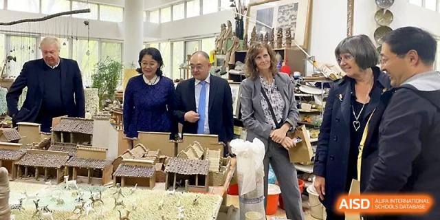Three adults in professional attire stand behind a table featuring student-made architectural models at WeiFang No.1 Middle School.