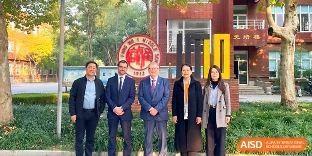 A group of five professionals stand outside a red brick school building for a commemorative group portrait at WeiFang No.1 Middle School.