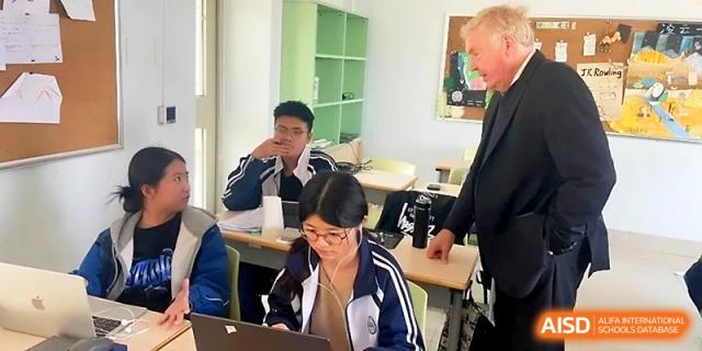 An instructor stands by a student's desk in a classroom, offering guidance as the student works on a laptop at WeiFang No.1 Middle School.