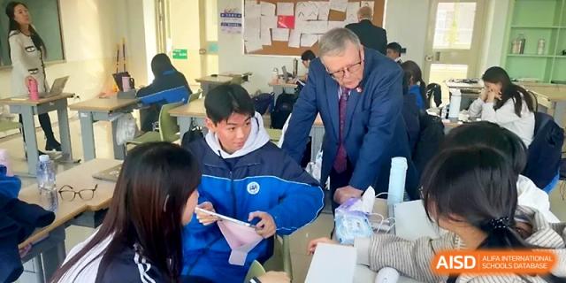 An educator in a blue suit leans over to assist a student with a hands-on activity in a bright classroom at WeiFang No.1 Middle School.