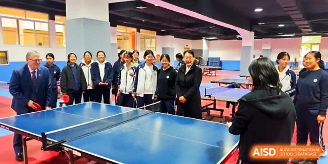 Students and a teacher gather around blue ping-pong tables in an indoor sports facility at WeiFang No.1 Middle School.