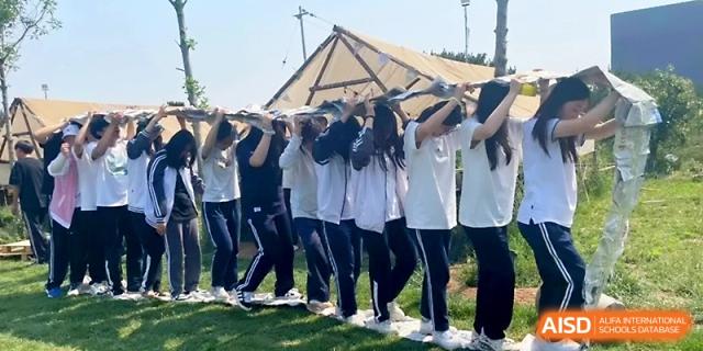 Students in school uniforms participate in a team-building exercise by holding a long banner over their heads outdoors at WeiFang No.1 Middle School.