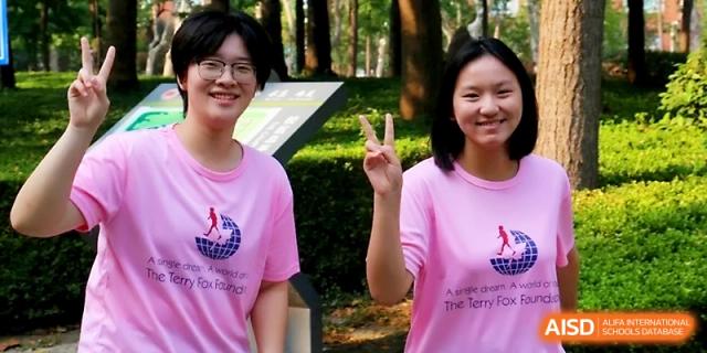 Two students in pink t-shirts pose for a photo outdoors, one making a peace sign during a school event at WeiFang No.1 Middle School.