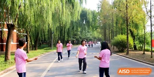 A group of students in pink shirts run down a tree-lined path during an outdoor athletic activity at WeiFang No.1 Middle School.