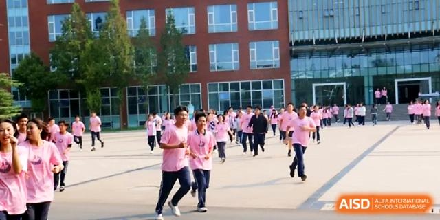 Large groups of students wearing pink t-shirts run across an open courtyard in front of a modern brick building at WeiFang No.1 Middle School.
