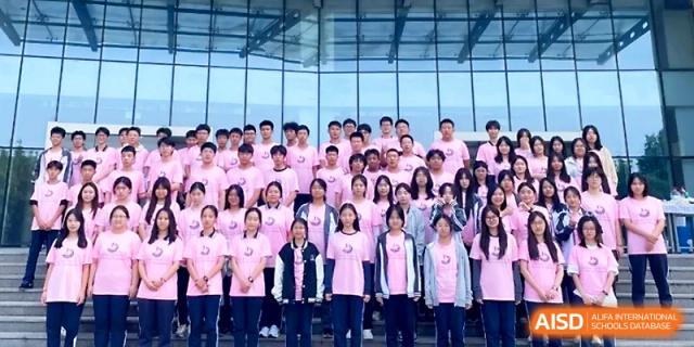 A large group of students in pink event shirts pose for a formal group portrait on a set of stairs at WeiFang No.1 Middle School.