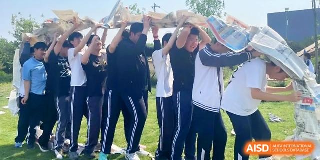 A line of students works together to carry a long, flat object over their heads during an outdoor team challenge at WeiFang No.1 Middle School.