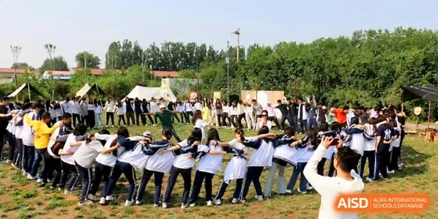 A large circle of students in school jackets participate in a rhythmic group activity on a grassy field at WeiFang No.1 Middle School.