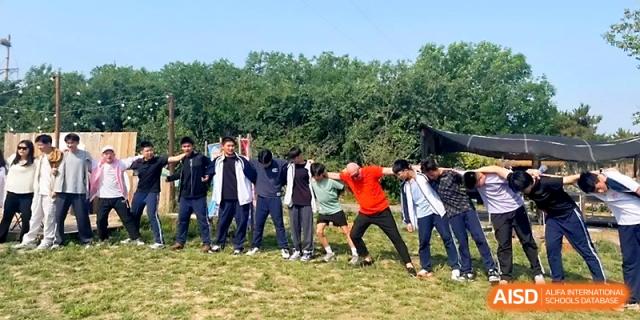 Students participate in a fun outdoor coordination game, leaning and reaching while standing in a line at WeiFang No.1 Middle School.
