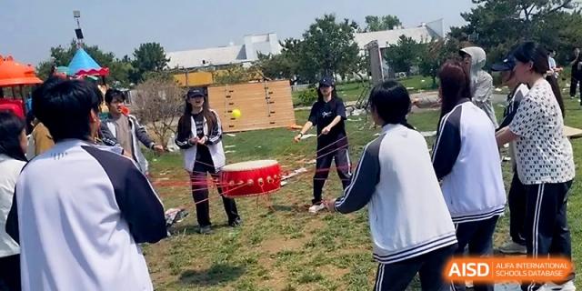 Students participate in a traditional drum activity outdoors, using ropes to balance and play the instrument at WeiFang No.1 Middle School.