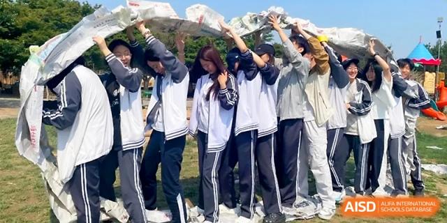 A team of students works together to hold up a long, decorated banner during an outdoor field day event at WeiFang No.1 Middle School.