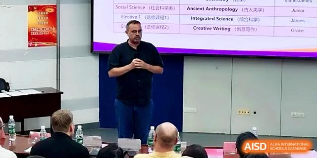 A speaker addresses a group from the front of a lecture room, with a course schedule displayed on the screen at Wuhan No.2 High School.