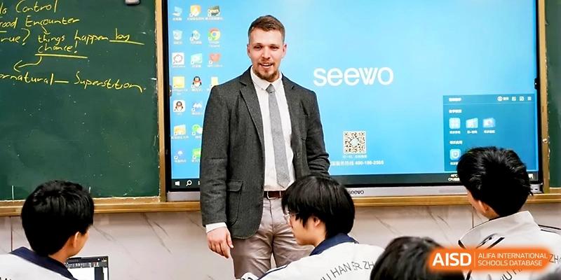 A teacher in a grey blazer stands in front of a digital whiteboard, preparing to start a technical presentation at Wuhan No.2 High School.