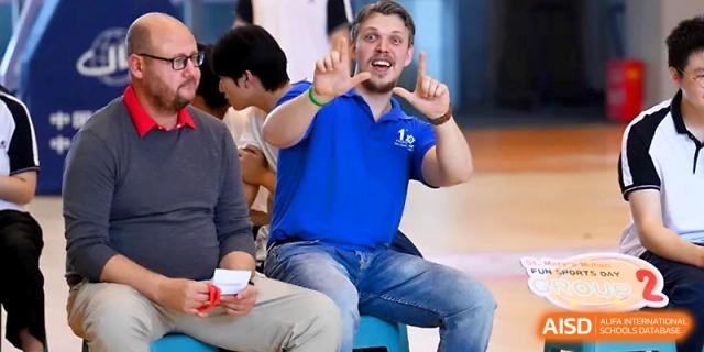 An enthusiastic male staff member gestures cheerfully while sitting with a group during a school event at Wuhan No.2 High School.