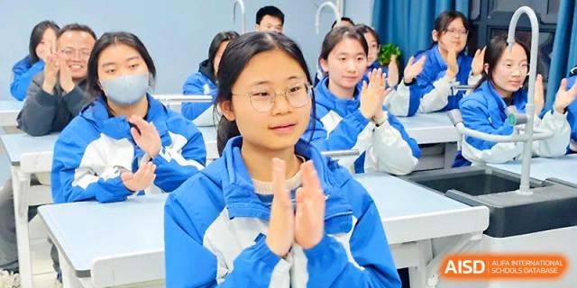 A student in a blue and white uniform claps during a classroom presentation with classmates in the background at Xi_an Bodi School.