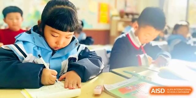 A young student focuses on writing in their notebook during a quiet classroom lesson at Xi_an Bodi School.