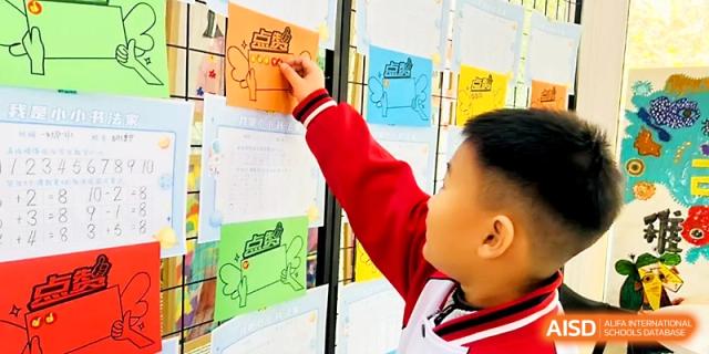 A student in a red and white uniform pins a drawing onto a classroom display board at Xi_an Bodi School.