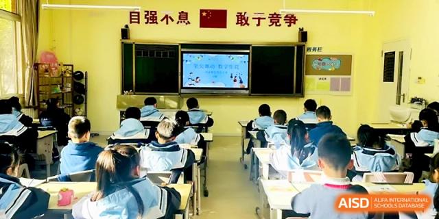 A wide shot of a classroom with students seated at desks facing a digital screen for a lesson at Xi_an Bodi School.