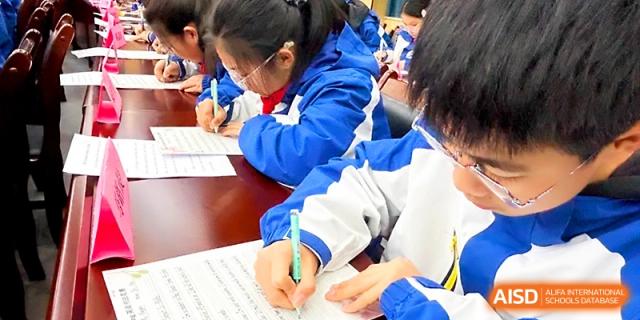Students in blue uniforms participate in a group writing activity or exam in a large hall at Xi_an Bodi School.