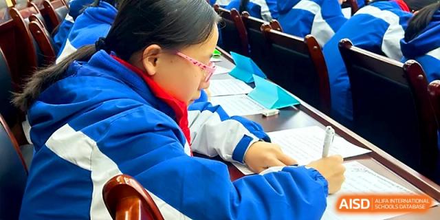 A girl with glasses focuses on her paperwork during a quiet study session or competition at Xi_an Bodi School.
