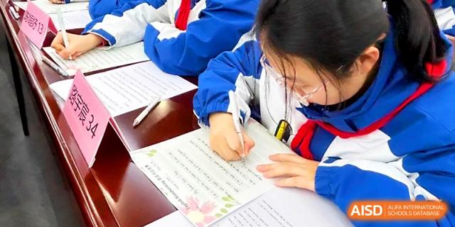 A close-up of a student carefully writing a letter or essay on a decorated sheet of paper at Xi_an Bodi School.