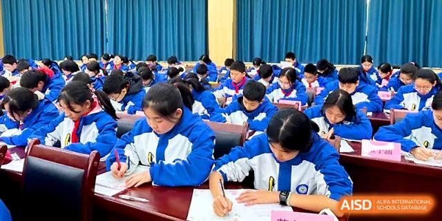 A large group of students in blue jackets works on an assignment together in a spacious room at Xi_an Bodi School.