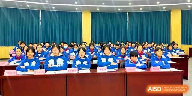 A large group of students in blue jackets sits attentively in an auditorium during a school assembly at Xi_an Bodi School.