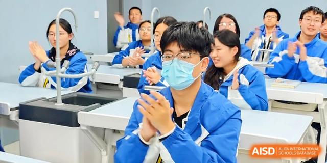 A student wearing a face mask claps while participating in a classroom discussion with peers at Xi_an Bodi School.
