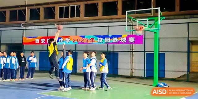 A group of boys plays basketball on a green court in front of a colorful school event banner at Xi_an Bodi School.
