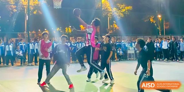 A student in a pink jersey performs a layup during an evening basketball game on the school court at Xi_an Bodi School.