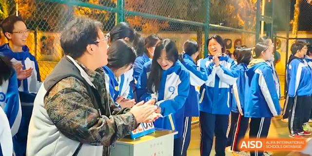 Students and a teacher cheer enthusiastically from the sidelines during an outdoor sports match at Xi_an Bodi School.