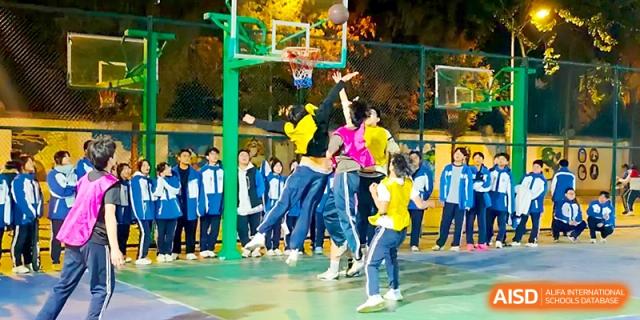 Students jump toward a basketball hoop during a competitive game on the outdoor court at Xi_an Bodi School.