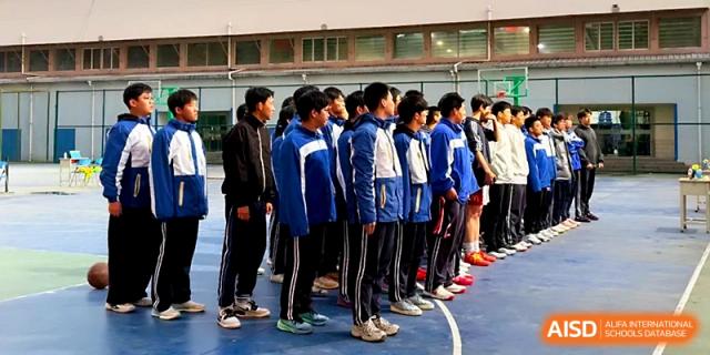 A group of male students stands together on the edge of a sports field during an outdoor event at Xi_an Bodi School.