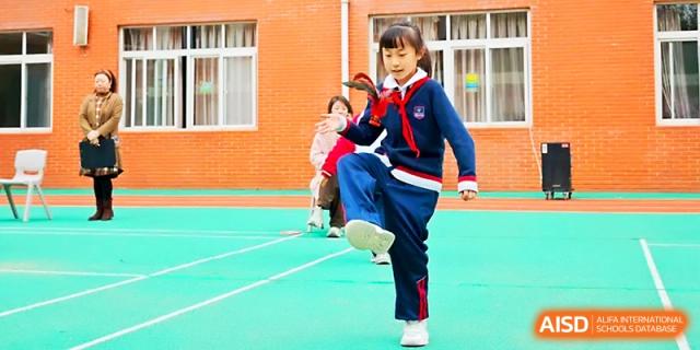 A student performs a balanced move while playing an outdoor game on the green sports surface at Xi_an Bodi School.