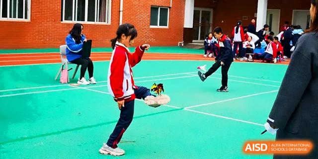 A young girl in a red jacket practices a traditional shuttlecock kicking game on the school court at Xi_an Bodi School.