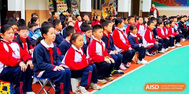 Rows of young students in red and white uniforms sit and watch a performance on the sports field at Xi_an Bodi School.