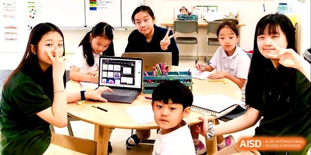 A teacher assists young students with a digital tablet and writing assignments at a wooden table at Xi_an Hanova International School.