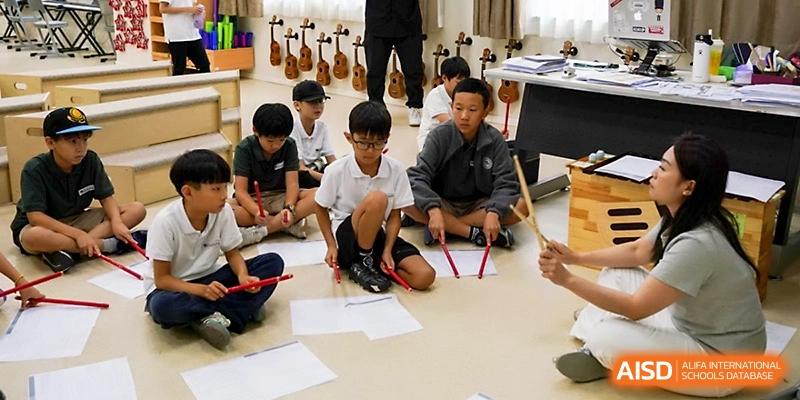 Students sit in a circle on the floor during a music class with percussion instruments and papers at Xi_an Hanova International School.