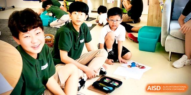 Two boys in school uniforms look toward the camera while working on an art or writing project on the floor at Xi_an Hanova International School.