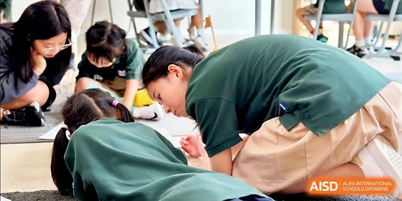 A student in a green shirt leans over a large sheet of paper to draw or write during a creative lesson at Xi_an Hanova International School.