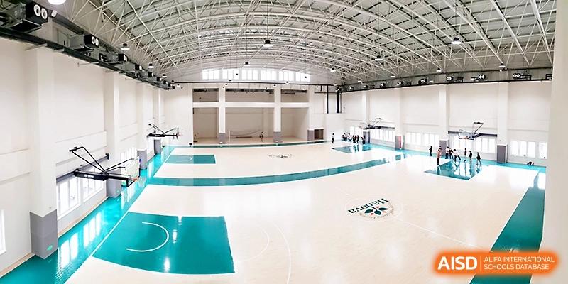 An expansive view of a modern, high-ceilinged indoor gymnasium with polished basketball courts at Xi_an Hanova International School.