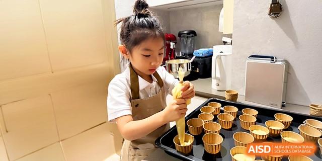 A girl wearing a beige apron carefully prepares cupcakes during a school baking session at Xi_an Hanova International School.