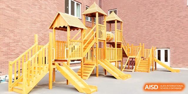 A large wooden outdoor playground structure with slides for student play and exercise at Xi_an Hanova International School.