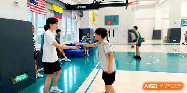 Two students share a friendly high-five during a physical education class in the gymnasium at Xi_an Hanova International School.