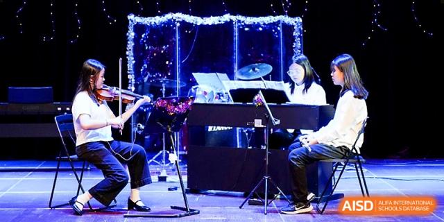 Students perform music on a stage with a piano and drums under bright blue stage lighting at Xi_an Hanova International School.